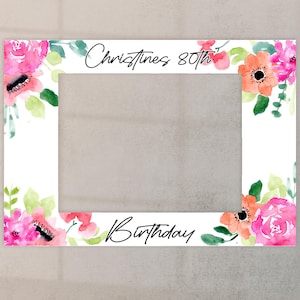 May include: A white photo booth frame adorned with watercolour flowers in shades of pink, orange, and green. The text "Christines 80th Birthday" is written in black script across the top and bottom of the frame.