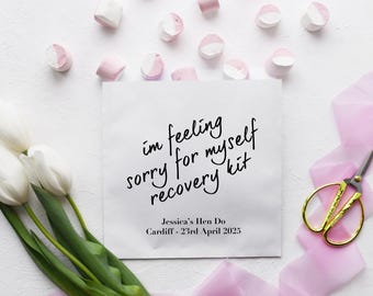 May include: White paper bag with the text "I'm feeling sorry for myself recovery kit" and the text "Jessica's Hen Do Cardiff - 23rd April 2025". The bag is surrounded by pink marshmallows, white tulips, and pink ribbon.