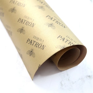 K&ouml;nnte beinhalten: Eine Rolle braunes Kraftpapier Geschenkpapier mit einem sich wiederholenden Muster aus schwarzen Bienen und dem aufgedruckten Text "Tequila Patron".
