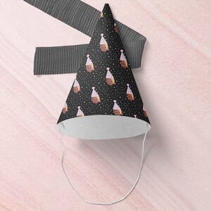 May include: A black and white party hat with a repeating pattern of a child's face wearing a pink party hat. The hat has a white interior and a white string attached to the bottom.