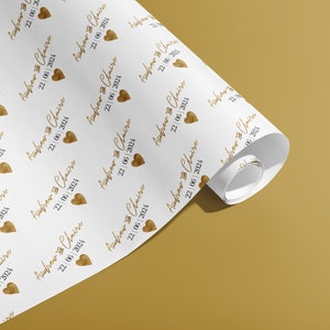K&ouml;nnte beinhalten: Wei&szlig;es Geschenkpapier mit einem sich wiederholenden Muster aus goldenen Herzen und dem Text "Andrew & Claire 22/06/2024".