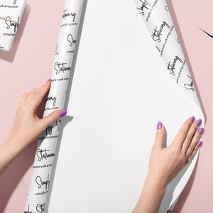 May include: White wrapping paper with a repeating pattern of the text "Simply Stationery" and the website address "simplystationeryuk.etsy.com". A person is wrapping a gift with the paper.