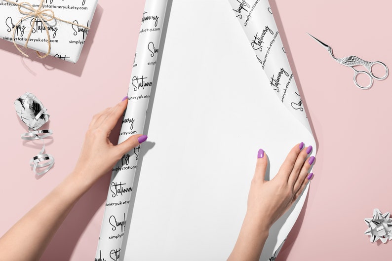 May include: White wrapping paper with a repeating pattern of the text "Simply Stationery" and the website address "simplystationeryuk.etsy.com". A person is wrapping a gift with the paper.