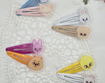 May include: A collection of colorful hair clips featuring cartoon animal faces. The clips are in various colors, including blue, pink, white, tan, purple, orange, and yellow. Each clip has a different animal design, such as a bunny, dog, and bear.