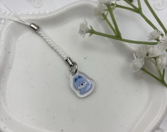 May include: A clear acrylic charm with a light blue cartoon dog design. The charm is attached to a white braided cord with a silver-colored metal clasp. The charm is on a white ceramic dish.