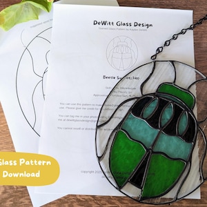 May include: Stained glass beetle suncatcher with green and black details, suspended by a black chain. The design is on a white background with a clear border. Includes a printed pattern for digital download.