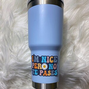 May include: A light blue stainless steel tumbler with a colorful sticker that reads "I'm nice pero no te pases" with a daisy graphic.