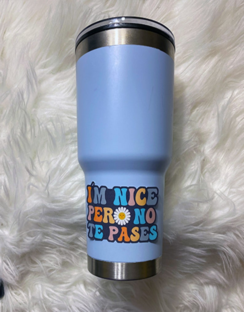 May include: A light blue stainless steel tumbler with a colorful sticker that reads "I'm nice pero no te pases" with a daisy graphic.