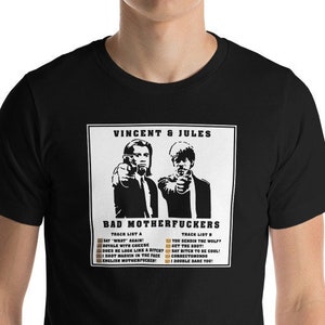 May include: Black t-shirt featuring a graphic of two men pointing guns, with the text "VINCENT & JULES" and "BAD MOTHERFUCKERS". Below the image are two lists of song titles. The shirt is made of a soft material.