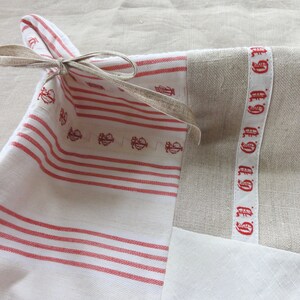 Könnte beinhalten: Ein rechteckiger Stoffkorb mit rot-weiß gestreiftem Stoff und einer beigen Schleife. Der Korb hat eine beige Leineninnenseite und ein weißes Band mit roten Buchstaben.
