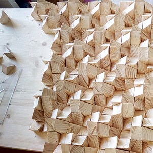 May include: A wall panel made of many small, light brown wooden pieces arranged in a geometric pattern. The pieces are all different sizes and shapes, and they create a unique and interesting texture.