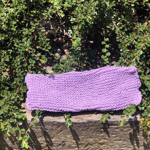 Puede incluir: Un paño de cocina de punto de color lavanda, hecho con un patrón de punto sencillo, está sobre una superficie de madera desgastada.