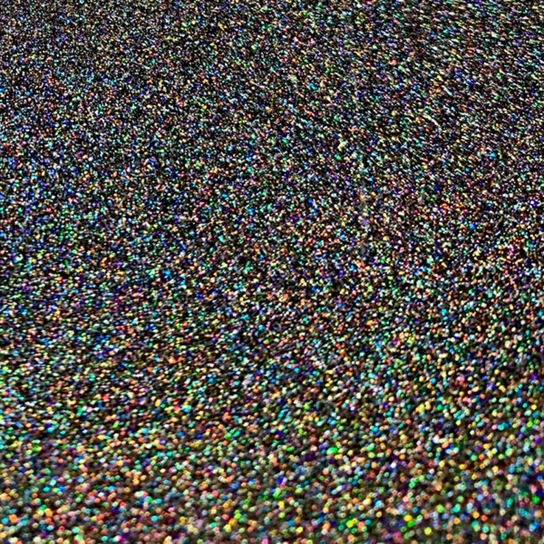 May include: Close-up of a surface covered in small, iridescent glitter particles. The glitter has a dark base color with a shimmering, rainbow effect. The overall appearance is textured and sparkling.