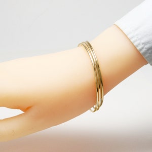K&ouml;nnte beinhalten: Drei goldene Armreifen, die auf einem Handgelenk &uuml;bereinander liegen. Die Armreifen sind schlicht und haben eine polierte Oberfl&auml;che.
