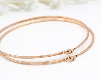 May include: Two delicate, rose gold bangles with hammered texture and secure clasp closures. The bracelets are displayed on a white background, showcasing their simple elegance. These are ideal for everyday wear.