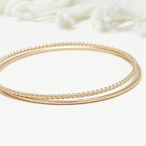 May include: Two gold bangles, one with a twisted design and the other with a smooth finish.