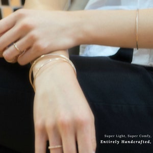 K&ouml;nnte beinhalten: Ein Set aus drei d&uuml;nnen goldenen Armb&auml;ndern, die am Handgelenk einer Person &uuml;bereinander liegen. Die Armb&auml;nder sind schlicht und zart, mit einer glatten, polierten Oberfl&auml;che. Der Text "Super Light, Super Comfy, Entirely Handcrafted" ist am unteren Rand des Bildes sichtbar. Ringe erh&auml;ltlich bei IrresistiblyMinimal.etsy.com. Armb&auml;nder erh&auml;ltlich bei IrresistiblyMinimal4.etsy.com.