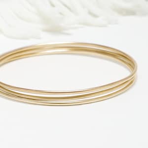 May include: Three gold bangles stacked on top of each other. The bangles are smooth and shiny.