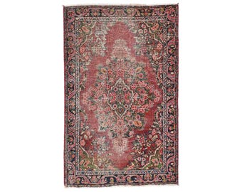 May include: Rectangular, vintage-style rug with a central floral medallion in shades of red, pink, and green. The rug features a dark border with floral patterns and a distressed appearance, suggesting age and use. The rug is suitable for home decor.