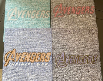 May include: Four pieces of paper with the Avengers logo written in different colors. The logos are "Avengers", "Avengers Age of Ultron", "Avengers Infinity War", and "Avengers".