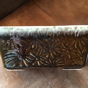 May include: A brown ceramic planter with a white glaze and a floral design. The planter has a rectangular shape and a slightly raised rim.