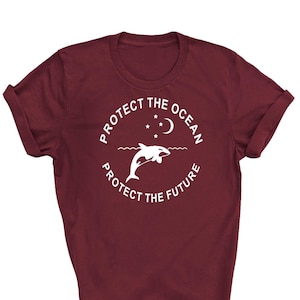 May include: A maroon t-shirt with a white circle graphic featuring a dolphin jumping out of the water with a crescent moon and stars above. The text "Protect the Ocean" is written around the top of the circle and "Protect the Future" is written around the bottom of the circle.