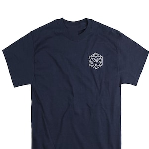 May include: A navy blue short-sleeve t-shirt featuring a white line-art graphic of a twenty-sided die on the upper left chest. The die displays various numbers, with the number 20 prominently centered within the geometric shape.