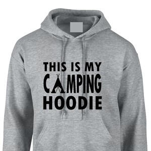 May include: A gray hooded sweatshirt with the text "THIS IS MY CAMPING HOODIE" in black. The design includes a tent graphic. The hoodie has a front pocket and a drawstring hood.
