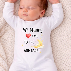 May include: A sleeping baby wearing a white onesie with the text "MY Nanny ❤️'s ME TO THE AND BACK!" The design includes a red heart, a smiling moon, and yellow stars. The baby is lying on a cream-colored blanket.
