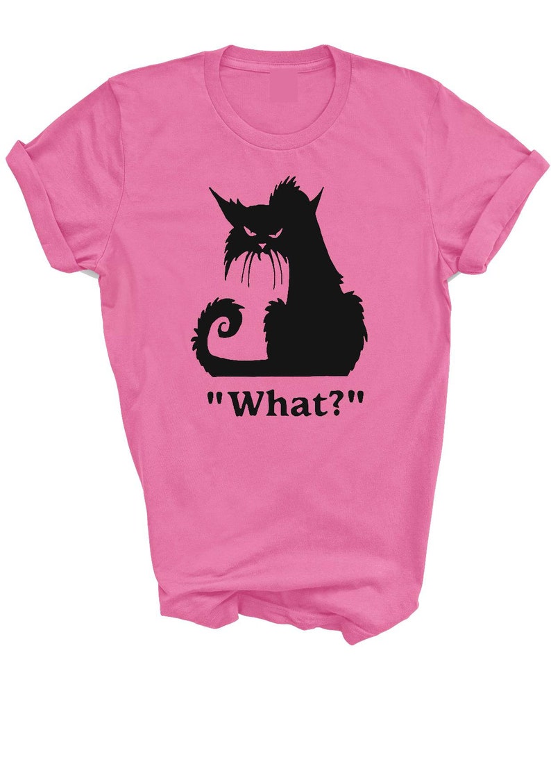 May include: Pink t-shirt featuring a black silhouette of a cat with an angry expression. The cat has pointed ears, a long tail, and a mustache. Below the cat is the word "What?" in black text.