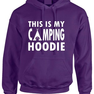 May include: A purple hoodie with a front pocket and a drawstring hood. The white text on the front reads "THIS IS MY CAMPING HOODIE" with a tent graphic. The hoodie is made of a soft material.