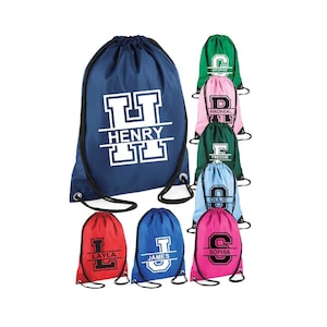 May include: A set of nine personalised drawstring bags in various colours. Each bag features a large letter and a name printed on the front. The bags are made of a durable, water-resistant material and are perfect for carrying books, clothes, or other personal items.