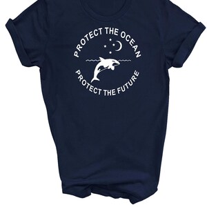 May include: Navy blue t-shirt with a white graphic of a dolphin jumping out of the water with a crescent moon and stars above. The text "Protect the Ocean Protect the Future" is written in a circle around the dolphin.
