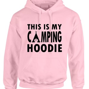 May include: A light pink hoodie with a front pocket and a drawstring hood. The black text on the front reads "THIS IS MY CAMPING HOODIE" with a tent graphic. The hoodie is made of a soft material.