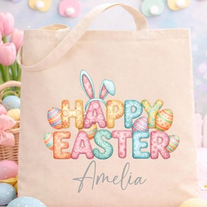 May include: Beige canvas tote bag with the words "HAPPY EASTER" in colorful, patterned letters, bunny ears, and Easter eggs. The name "Amelia" is written below the text in a cursive font. The background includes pastel Easter decorations.
