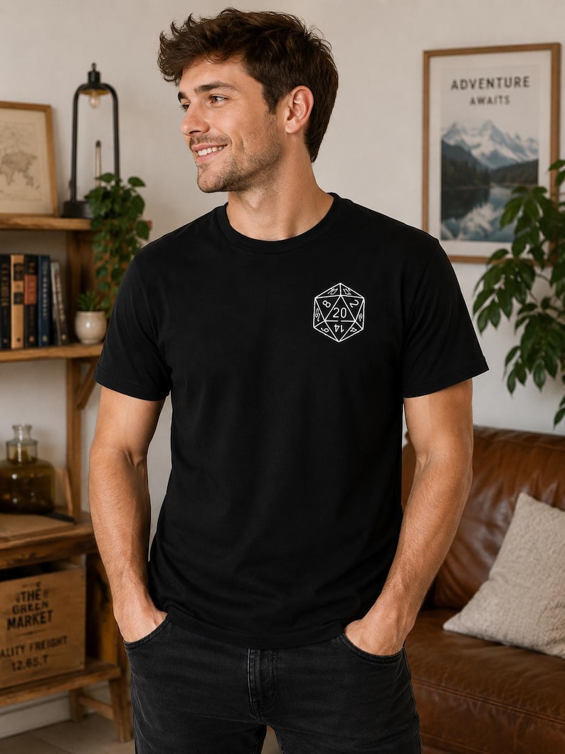 May include: A black short-sleeved t-shirt featuring a white line art graphic of a twenty-sided die on the left chest. The die design displays various numbers, with the number 20 prominently featured at the top center of the geometric shape.