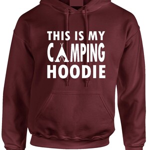 May include: A maroon hoodie with a front pocket and a drawstring hood. The white text on the front reads "THIS IS MY CAMPING HOODIE" with a tent graphic. A comfortable garment for outdoor enthusiasts.