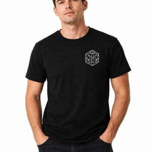 May include: A black short-sleeved t-shirt featuring a white line art graphic of a twenty-sided die on the left chest. The die design displays various numbers, with the number 20 prominently centered within the geometric shape of the polygon.