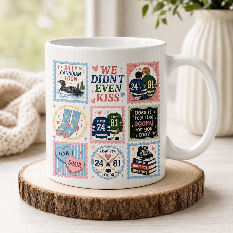 May include: A white ceramic mug featuring a grid of colorful illustrations including a loon, hockey jerseys with numbers 24 and 81, heart-shaped candies labeled Ilya and Shane, and text that reads WE DIDN'T EVEN KISS and Does it feel like agony for you too?