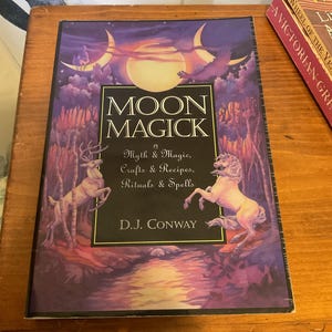 May include: A book titled Moon Magick by D.J. Conway with a purple and gold cover illustration featuring a full moon, a deer, and a horse. The text reads Moon Magick, Myth & Magic, Crafts & Recipes, Rituals & Spells, and D.J. Conway.