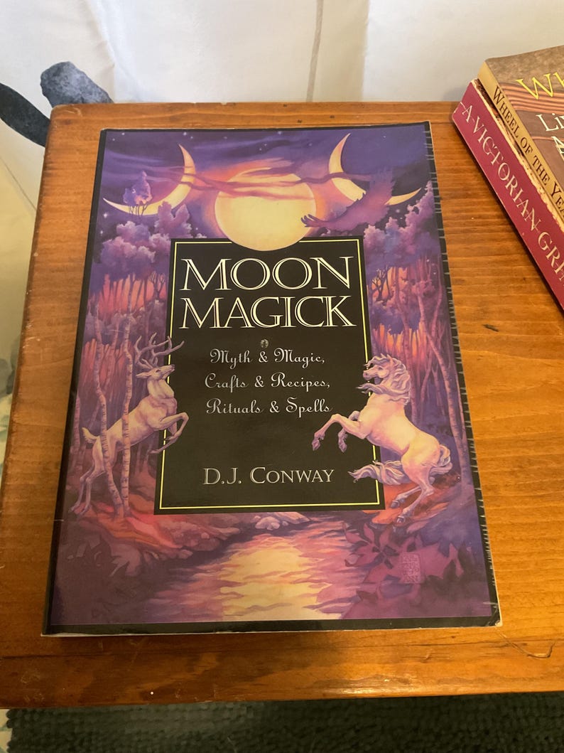 May include: A book titled Moon Magick by D.J. Conway with a purple and gold cover illustration featuring a full moon, a deer, and a horse. The text reads Moon Magick, Myth & Magic, Crafts & Recipes, Rituals & Spells, and D.J. Conway.