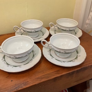 May include: Set of four white porcelain teacups and saucers with a green and gold floral design.