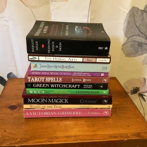May include: A vertical stack of ten books with various colored spines and titles including Drawing Down the Moon, The Herbal Arts, Jeanne Rose's Herbal Body Book, Spinning Spells, Tarot Spells, Green Witchcraft, Wicca, Moon Magick, and A Victorian Grimoire.