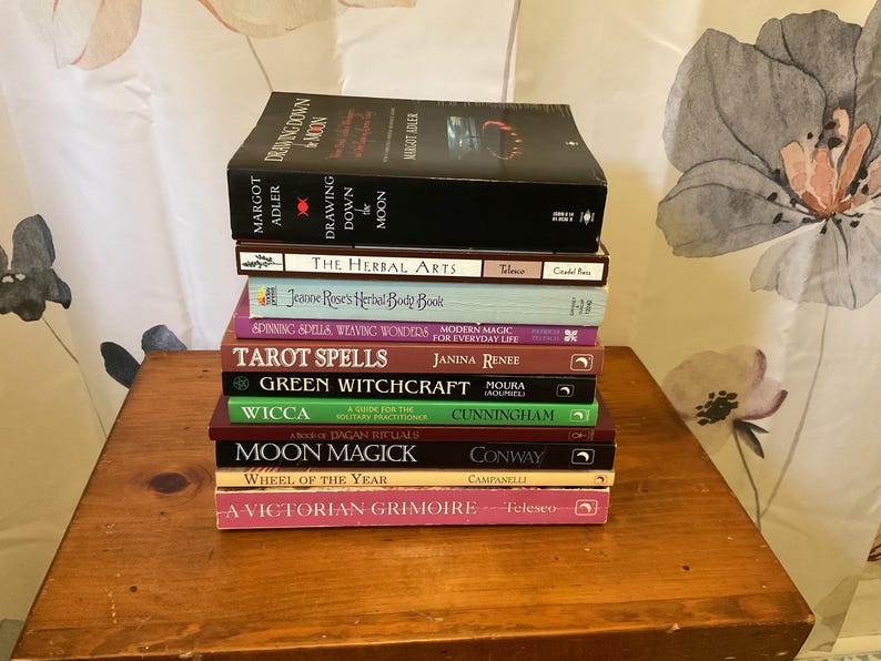 May include: A vertical stack of ten books with various colored spines and titles including Drawing Down the Moon, The Herbal Arts, Jeanne Rose's Herbal Body Book, Spinning Spells, Tarot Spells, Green Witchcraft, Wicca, Moon Magick, and A Victorian Grimoire.