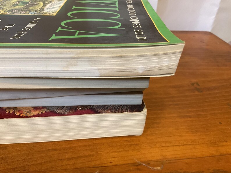 May include: A stack of three books with visible page edges. The top book has a black cover with green text reading WICCA and white text stating A GUIDE FOR THE SOLITARY PRACTITIONER and OVER 400,000 COPIES SOLD. The bottom book has a dark red cover.