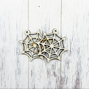 Peut inclure: Deux ornements en forme de toile d'araignée en bois découpé au laser. Chaque ornement est de couleur beige clair avec un trou circulaire en haut pour l'accrochage. Les toiles d'araignée ont un design détaillé avec des lignes rayonnantes et un centre circulaire.