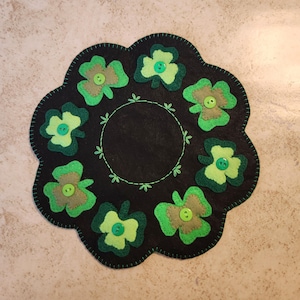 Peut inclure: Un dessous de plat en feutre noir avec un bord festonné, décoré de trèfles en feutre vert et de boutons verts. Un cercle et des feuilles verts cousus sont au centre. Le dessous de plat est pour la Saint-Patrick.