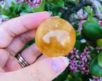 May include: A smooth, golden yellow citrine sphere crystal ball. The sphere is polished and reflects light.