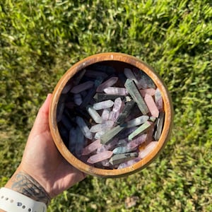 May include: A wooden bowl filled with a variety of colorful crystal points, including pink, green, purple, and black.