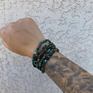 May include: A stack of turquoise and brown beaded bracelets on a person's wrist.